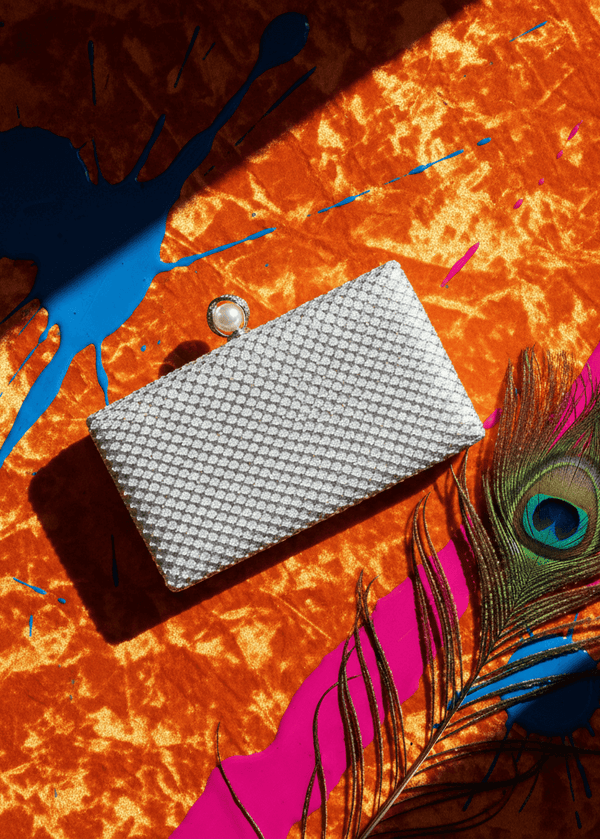 Clutch Crystal Pearl argintiu cu cristale și închizătoare perlă, pe fundal portocaliu vibrant cu pană de păun