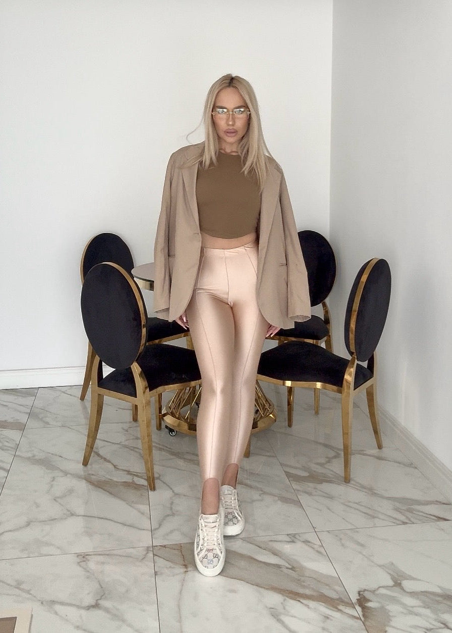 Femeie purtând colanți modelatori aurii, top bronz și sacou pe fundal elegant.