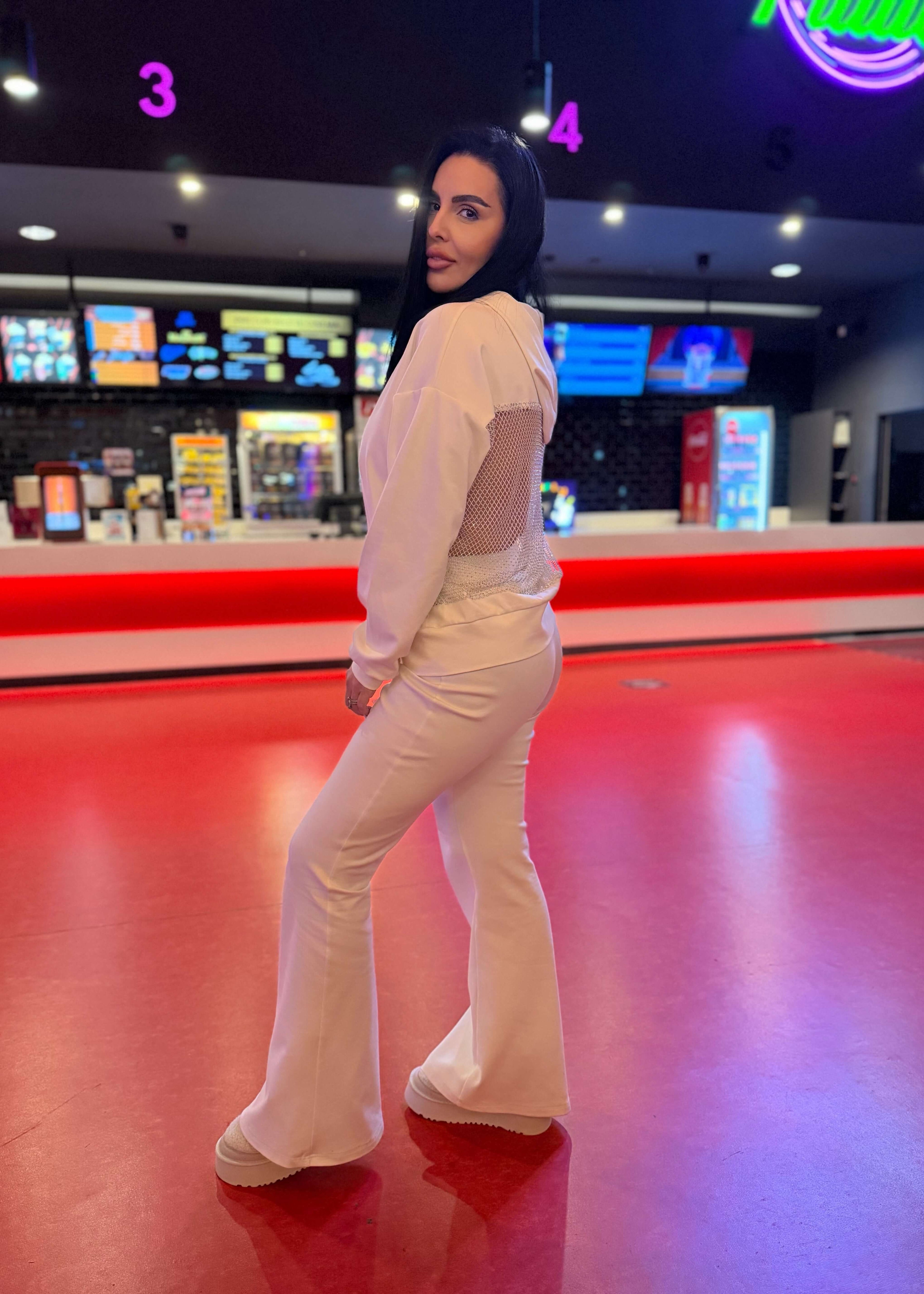 Femeie purtând SIA pantaloni tip trening FLARE albi, evazați, în locație modernă, iluminată, focus pe stil și confort.