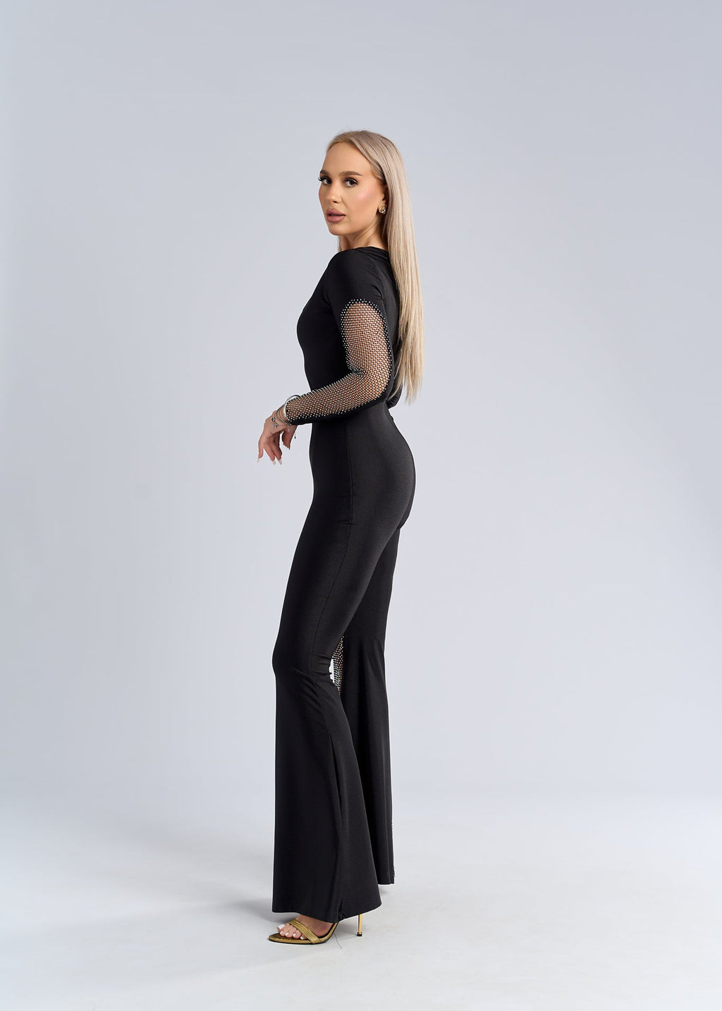 Salopetă neagră din lycra cu inserții din plasă strălucitoare, croială mulată și pantaloni evazați, vedere laterală pe model