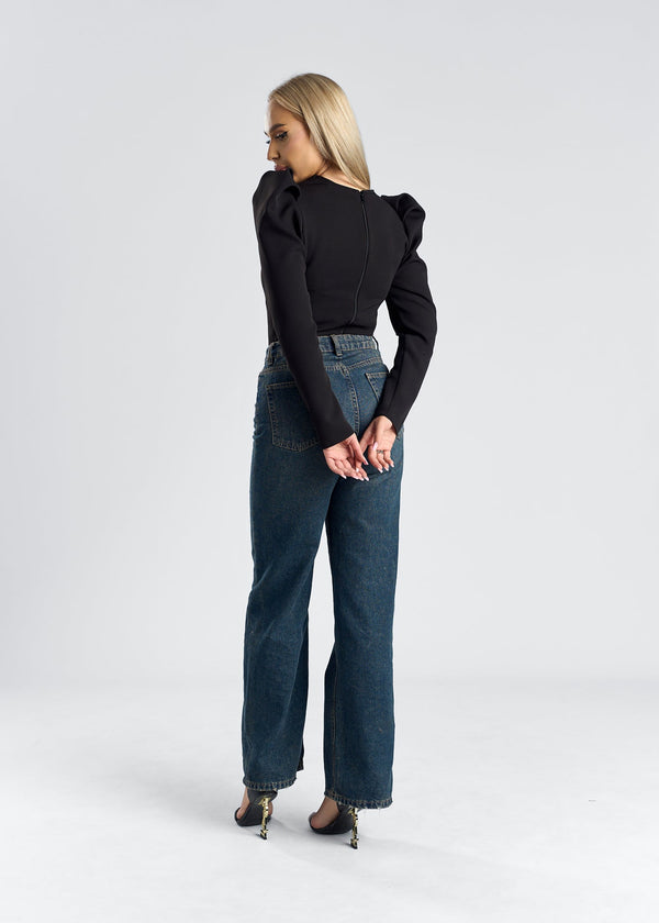 Top cu umeri supradimensionați, model elegant, purtat de femeie cu părul blond, jeans decoltați.