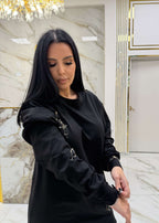 Hoodie negru "ATTITUDE" cu ace metalice, purtat într-o cameră cu decorațiuni luxoase